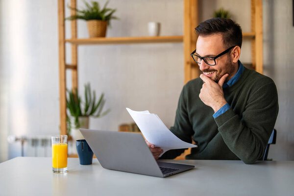 Улыбающийся бизнесмен-аналитик-бухгалтер, хранящий документы, работающий за ноутбуком, проводящий исследования в области технологий онлайн-торговли.