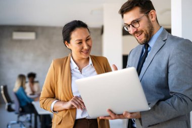 Ofiste yeni bir proje üzerinde çalışırken gülen iş adamları. Modern bir çalışma alanında çalışırken bilgisayar kullanan bir grup farklı iş adamı..