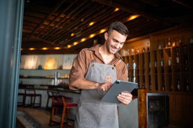 Proud cafe owner young man standing confidently behind the counter, ready to serve customers with a warm smile