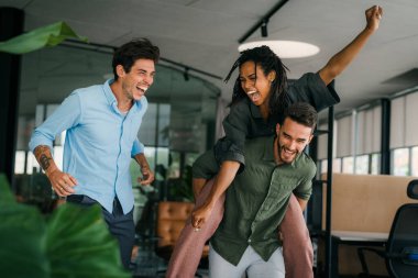 Yaratıcı modern ofisteki aşırı neşeli genç çalışanların portresi. Gülümseyen çok ırklı meslektaşlar, ortak iş başarısını veya görevde kazandığı zaferi kutluyor.