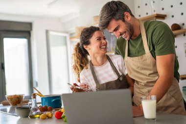 Genç kadın ve erkek online aşçılık atölyesine katılmak için dizüstü bilgisayar kullanıyor, internetten vegan mutfak tarifleri öğreniyorlar. İnternette yemek kursunu izleyen mutlu çift.