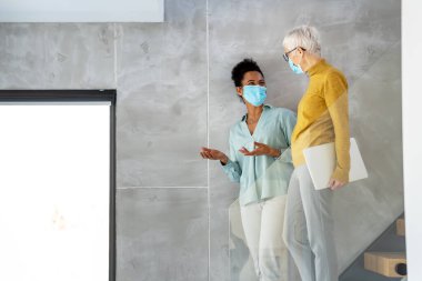 Teknoloji, yapay zeka, dijital yenilik ve salgın zamanlarında güvenli işyeri işbirliği için dizüstü bilgisayar kullanan maskeli kadın profesyoneller