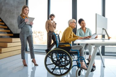 Tekerlekli sandalyedeki engelli kadın bilgisayara bakıyor, ırklar arası projeyi tartışıyor. Katılım, eşitlik mutlu iş insanları konsepti