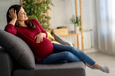 Mutlu hamile anne yatakta oturuyor, tekmelerini hissediyor, koca göbeğini okşuyor, gülümsüyor. Hamile kadın tokuşturuyor, doğmamış bebekle konuşuyor. Annelik, hamilelik kavramı