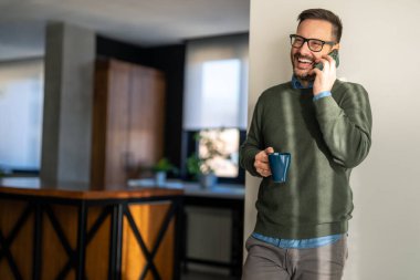 Mutlu gülümseyen iş adamı günlük kıyafetler giyer ve ev ofisinde modern akıllı telefon kullanır. İnsanlar dijital cihazlar modern yaşam konsepti