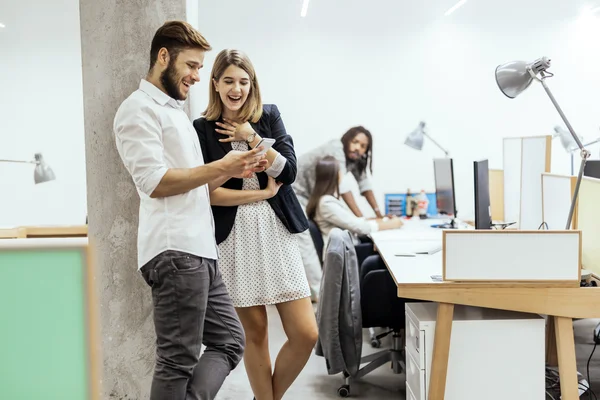 Kollegor i office använder telefoner och ler — Stockfoto