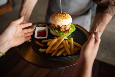 Hospitality in action, a smiling waiter serves a fresh burger and fries in a stylish restaurant, capturing the essence of great service and casual dining vibes