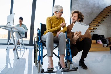 Tekerlekli sandalyedeki engelli kadın bilgisayara bakıyor, ırklar arası projeyi tartışıyor. Katılım, eşitlik mutlu iş insanları konsepti