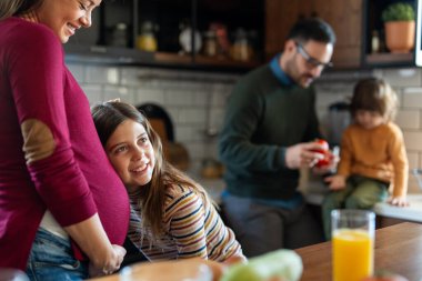 Mutlu kız, hamile annesinin karnına sarılıyor. Hamile bir kadını kucaklarken bebek hareketlerini dinleyen heyecanlı kız.