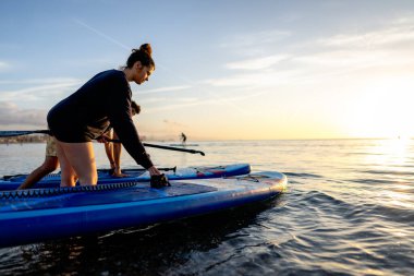 Güneş batarken kürekleri başında dinlenen iki insan, sakin, sağlıklı, sakin ve okyanusun rahatlatıcı ritmiyle dolu bir açık hava anı yaratıyor.