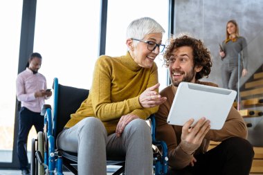 Farklı profesyonellerden oluşan bir grubun birlikte çalıştığı parlak, çağdaş bir ofis. Tekerlekli sandalye kullanan birini de kapsar.