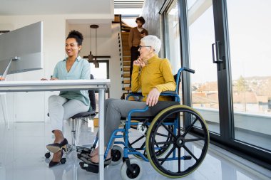 Tekerlekli sandalyedeki engelli kadın bilgisayara bakıyor, ırklar arası projeyi tartışıyor. Katılım, eşitlik mutlu iş insanları konsepti