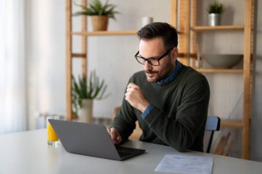 Elektronik bankacılık için akıllı telefon ve dizüstü bilgisayar kullanan, rezervasyon yapan, online alışveriş yapan ve evde vakit geçirirken ödeme yapan şık giyimli bir adam..