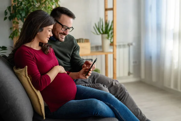 Mutlu çift evde sarılıp arkadaşlarıyla, aile üyeleriyle video görüşmesi yapıyor. Neşeli hamile kadın ve kocası iyi ruh hali içinde ailelerini selamlıyor, uygulamayla internet üzerinden iletişim kuruyor.