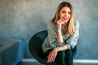 Yumuşak, modern bir iç mekanda gülümseyen rahat bir beyaz kadın, zarif, özgün ve doğal bir stil atmosferi olan sıcak bir yaşam tarzı portresi yaratıyor.