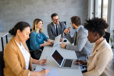 Ofiste yeni bir proje üzerinde çalışırken gülen iş adamları. Modern bir çalışma alanında çalışırken bilgisayar kullanan bir grup farklı iş adamı..