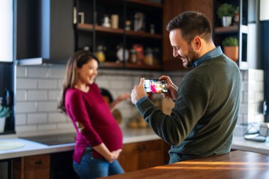 Mutlu çift evde sarılıp arkadaşlarıyla, aile üyeleriyle video görüşmesi yapıyor. Neşeli hamile kadın ve kocası iyi ruh hali içinde ailelerini selamlıyor, uygulamayla internet üzerinden iletişim kuruyor.