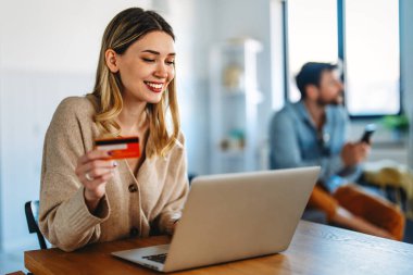 Evde dizüstü bilgisayar ve kredi kartı kullanan, çevrimiçi satışları, dijital pazarlamayı ve modern perakende teknoloji trendlerini temsil eden bir e-ticaret şirketinde çalışan gülümseyen kadın