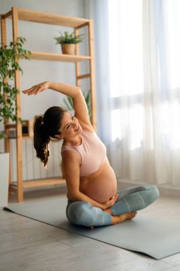 Çekici hamile kadın tozluklu ve etekli üstsüz oturma odasında yoga minderiyle egzersiz yapıyor. Denge, uyum ve hamilelik kavramı.
