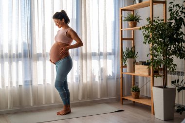 Güzel bir gülümsemesi olan, karnına el ele tutuşan, hamileliğinin son üç ayının tadını çıkaran çekici hamile bir kadın..