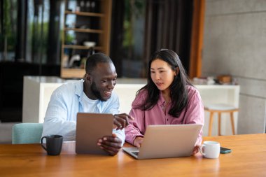 Mutlu Afrikalı Amerikalı ve Asyalı çift birlikte dizüstü bilgisayar kullanıyor, karı koca internetten alışveriş yapıyor, bilet alıyor, iyi haberler okuyor, boş zamanlarını geçiriyor.