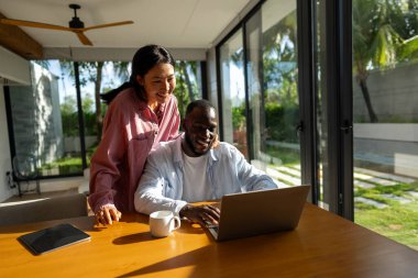 Başarılı çeşitlilik, çok ırklı bağımsız çift, birlikte dizüstü bilgisayarda çalışarak, tropik iklimin huzurlu ortamının tadını çıkarıyor..