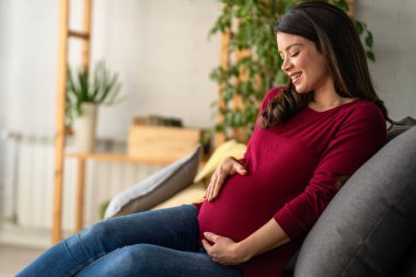 Hamile bir kadın yatakta rahat bir şekilde el ele tutuşurken görülüyor. Mutlu ve huzurlu görünüyor. Hamileliğinin son üç ayının tadını çıkarıyor..