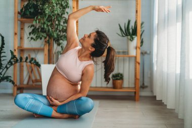 Evde çalışan hamile bir kadının portresi. Hamile kadın evde yoga yapıyor. Doğum öncesi kasıklar gerilir. Hamilelik yogası ve fitness.