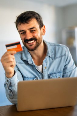 Evdeki dijital finans, güvenli işlemler ve modern finans yaşam tarzını temsil eden bir adam, kredi kartı ve dizüstü bilgisayarla online bankacılık yoluyla finansman yönetiyor.