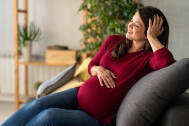Hamile bir kadın yatakta rahat bir şekilde el ele tutuşurken görülüyor. Mutlu ve huzurlu görünüyor. Hamileliğinin son üç ayının tadını çıkarıyor..