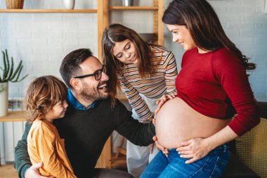 Hamile ve tatlı çocuklu mutlu bir aile evde eğleniyor ve birbirlerine sarılıyorlar. İnsanlar mutluluğu aile aşkı kavramı