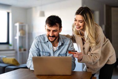 Mutlu çift internet bankacılığı aracılığıyla dijital finans, güvenli işlemler ve evdeki modern finans yaşam tarzını temsil eden bir kredi kartı ve dizüstü bilgisayarla finansman yönetiyor.