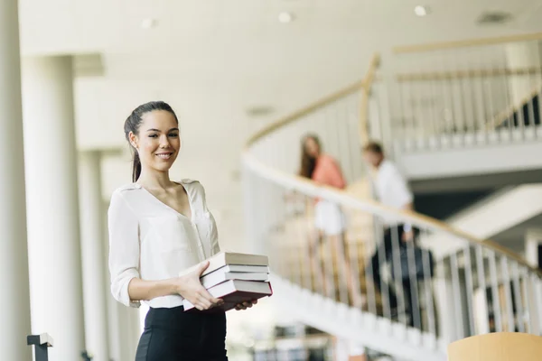 Hermosa mujer sosteniendo libros en una biblioteca — Foto de Stock