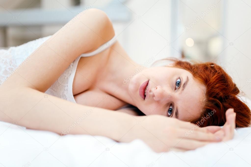 Beautiful red haired woman lying on bed