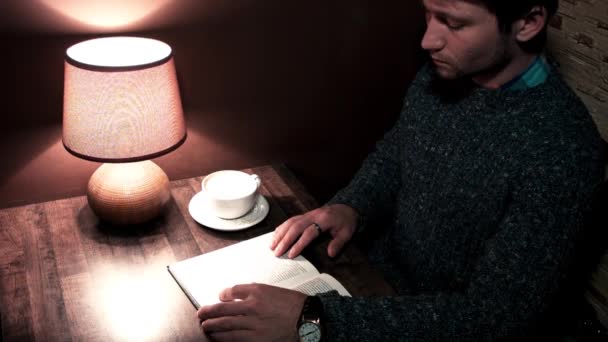 Der Typ am Schreibtisch liest ein Buch und trinkt Kaffee — Stockvideo