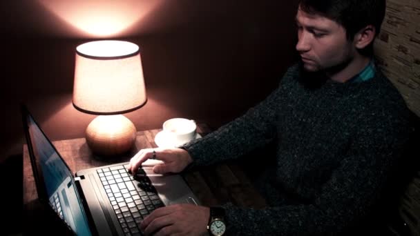 Человек, сидящий за столом и работающий на ноутбуке и пьющий кофе — стоковое видео