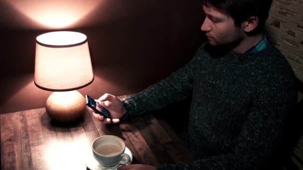 Man zit aan de tafel spelen op telefoon en drinken koffie — Stockvideo