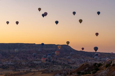 Kapadokya 'da güneş doğarken kayalık arazide uçan sıcak hava balonu. Seyahat