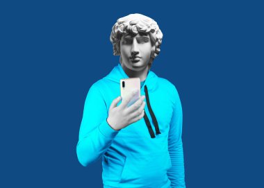 Modern art collage. Concept portrait of a man  holding mobile smartphone using app texting sms message. Gypsum head of Antinous. Man in suit. On a blue background. clipart