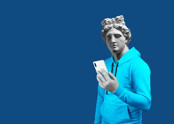 Modern sanat kolajı. Uygulama mesajlaşması mesajı kullanarak cep telefonu tutan bir adamın portresi. Apollo 'nun alçıtaşı başı. Takım elbiseli adam. Mavi bir arkaplanda.