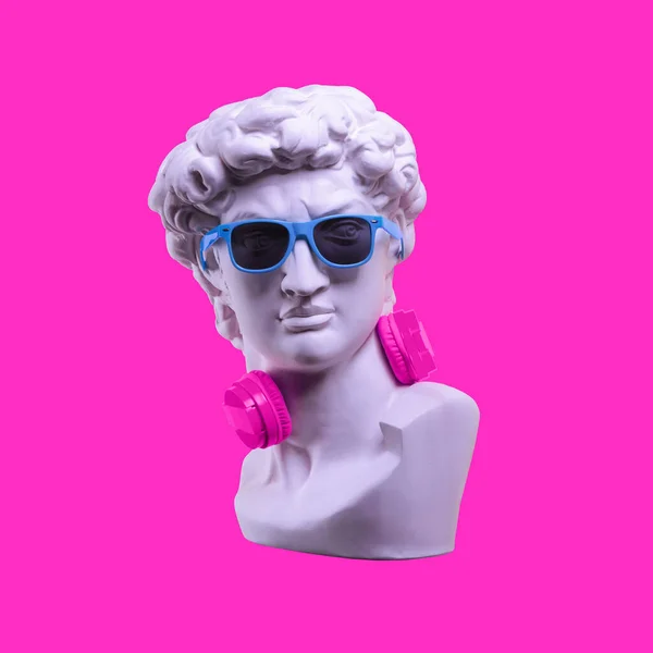 Heykel. Pembe arka planda kulaklık. David 'in kafasının alçıtaşı heykeli. Yaratıcı. David 'in mavi güneş gözlüklü heykeli. Asgari konsept sanat.