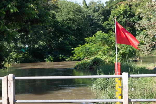 Red flag and yellow water level indicator in river to warn people of flooding — Stock Image Red Flag Yellow Water Level Indicator River Warn People Flooding Royalty Free Stock Photos