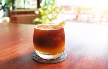 Yazın kafede, bir bardak siyah turuncu kahve, ahşap masada.