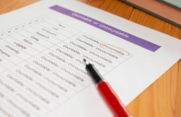 English grammar test sheet with red pen and clock on wooden table in classroom