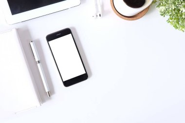 Not defteri, dizüstü bilgisayar ve kahve fincanı fare notlu üst görünüm ofis malzemeleri. Boş ekran cep telefonu ve beyaz masa çalışma alanı üzerindeki malzemeler ve kopyalama alanı.