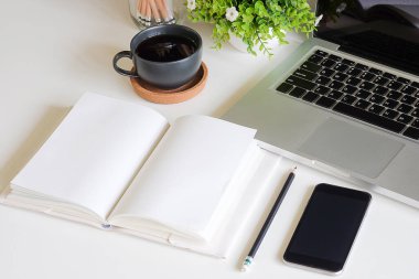Not defteri, dizüstü bilgisayar ve kahve fincanı fare notlu üst görünüm ofis malzemeleri. Boş ekran cep telefonu ve beyaz masa çalışma alanı üzerindeki malzemeler ve kopyalama alanı..