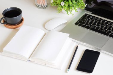 Not defteri, dizüstü bilgisayar ve kahve fincanı fare notlu üst görünüm ofis malzemeleri. Boş ekran cep telefonu ve beyaz masa çalışma alanı üzerindeki malzemeler ve kopyalama alanı..