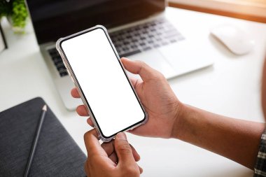 Modern ofisin bulanık arka planına sahip akıllı telefon kullanan erkek elleri yakın plan görüntüsü. Grafik görüntüleme için boş ekran monitörü.