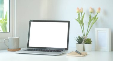 Simple workspace with white screen laptop, coffee cup and notebook on white table.	