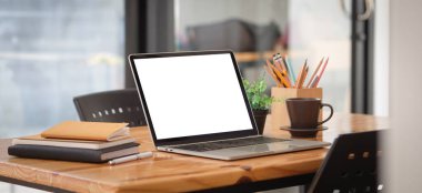 Laptop, dizüstü bilgisayar, kahve fincanı ve ahşap masadaki kırtasiye malzemesi ile basit bir iş yeri görüntüsünü kapat.